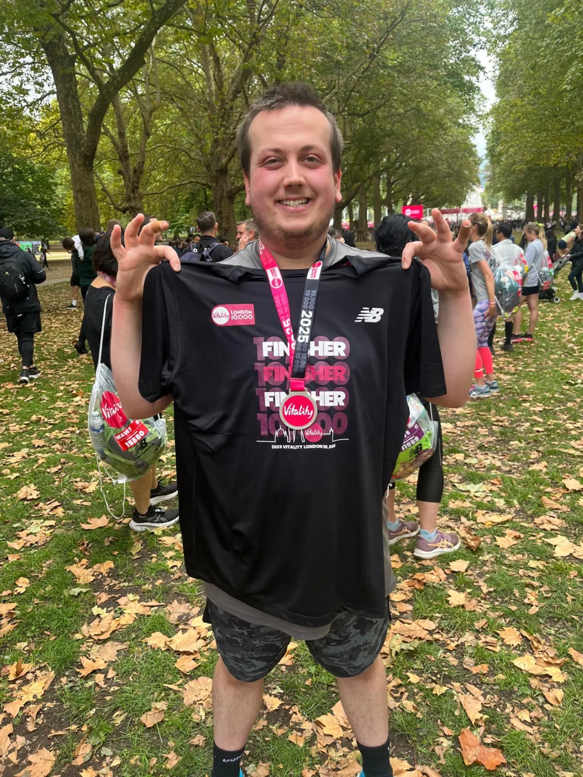 Eric holding up his black souvenir t-shirt, with a pink, black and silver medal around his neck.