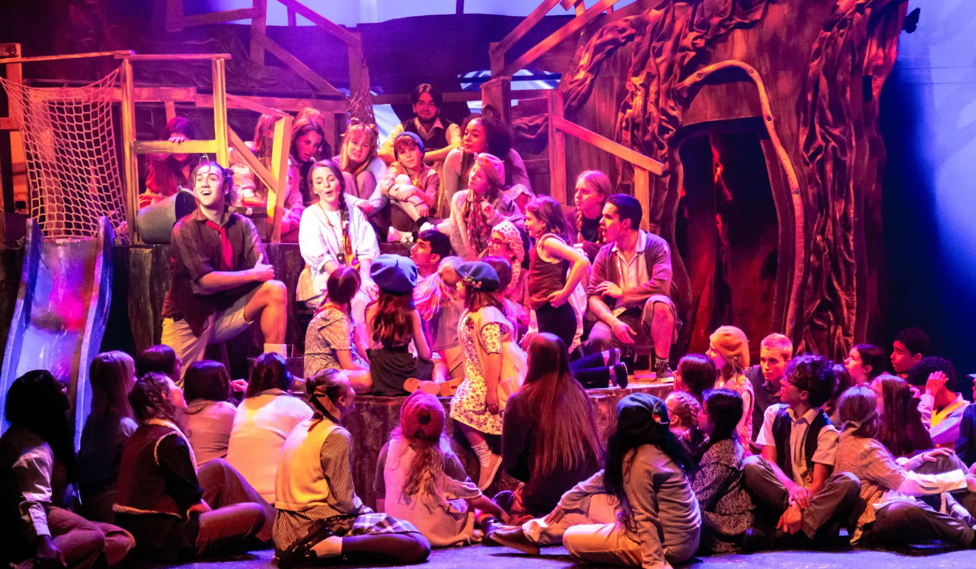 PAN performance 2024. Huge cast of young people on a stage in pink wash lighting.