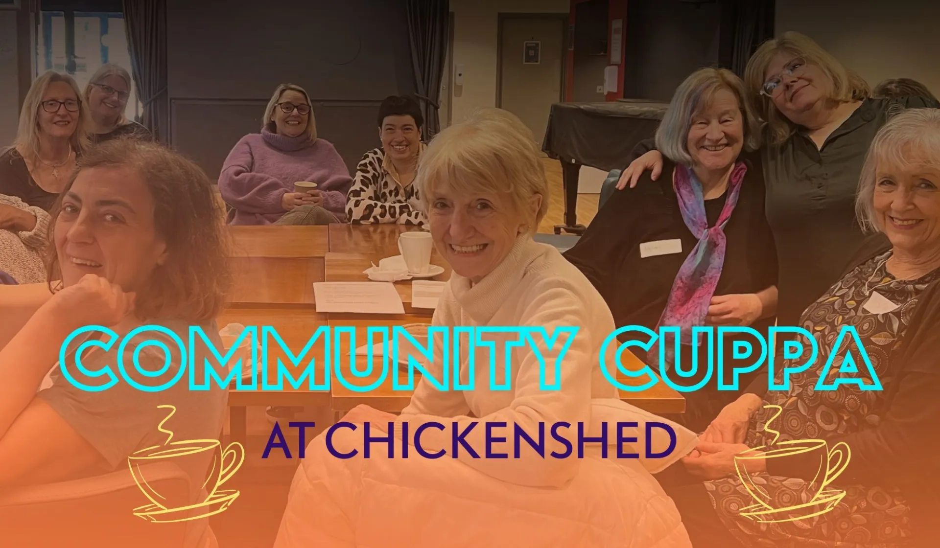 A diverse group of people sitting together in Chickenshed’s café, smiling and chatting around a table during a warm, inclusive Community Cuppa gathering.