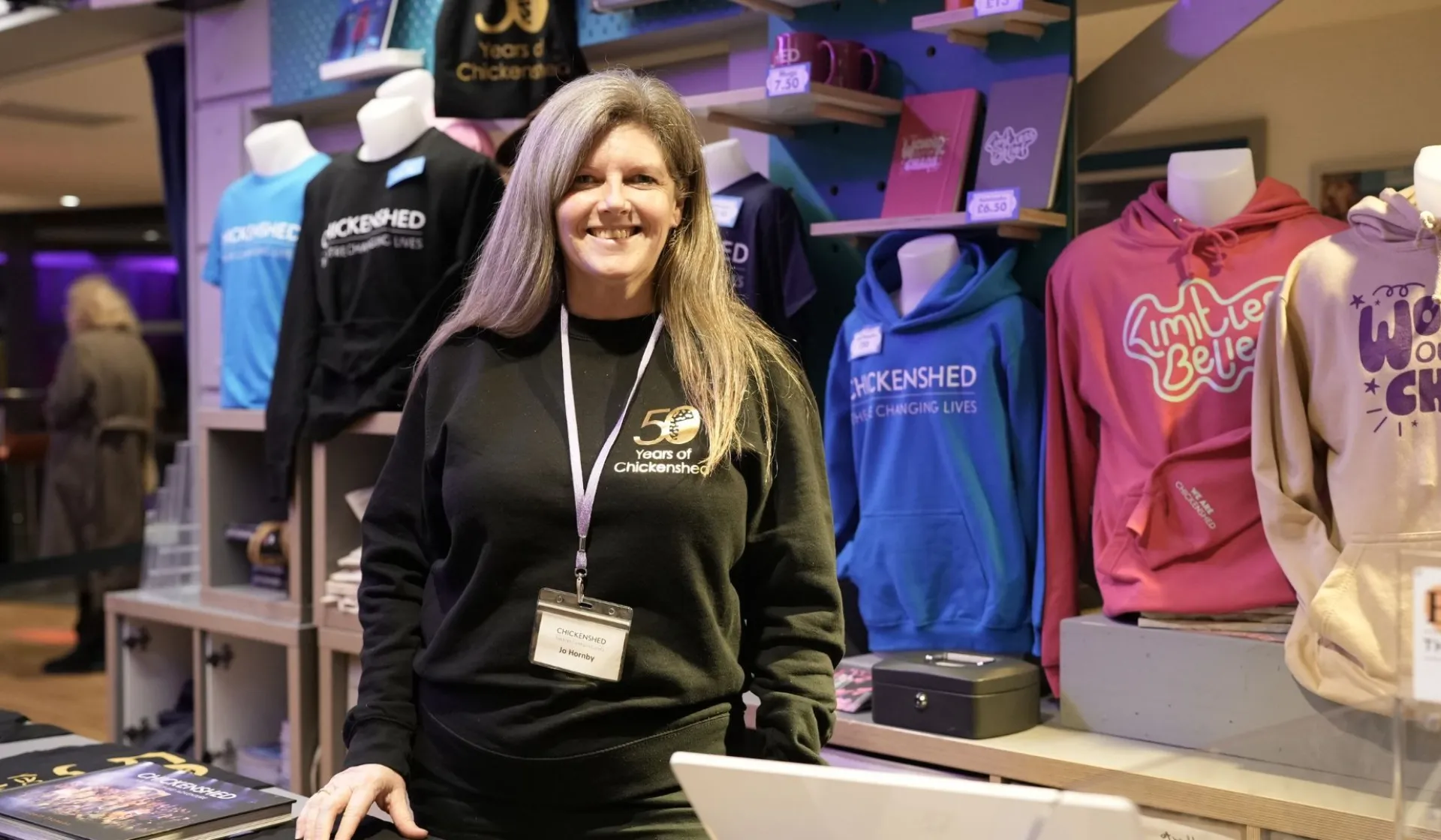 front of house woman standing at merchandise stand smiling