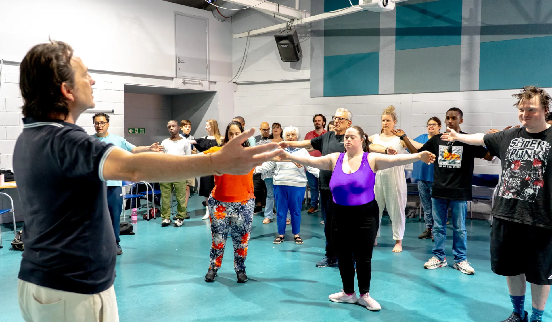 Teacher at the front of the room leading a arms out stretch to about 30 people