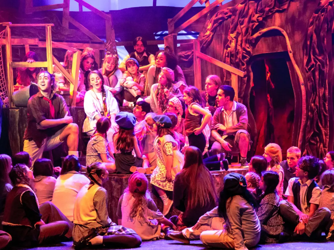 PAN performance 2024. Huge cast of young people on a stage in pink wash lighting.