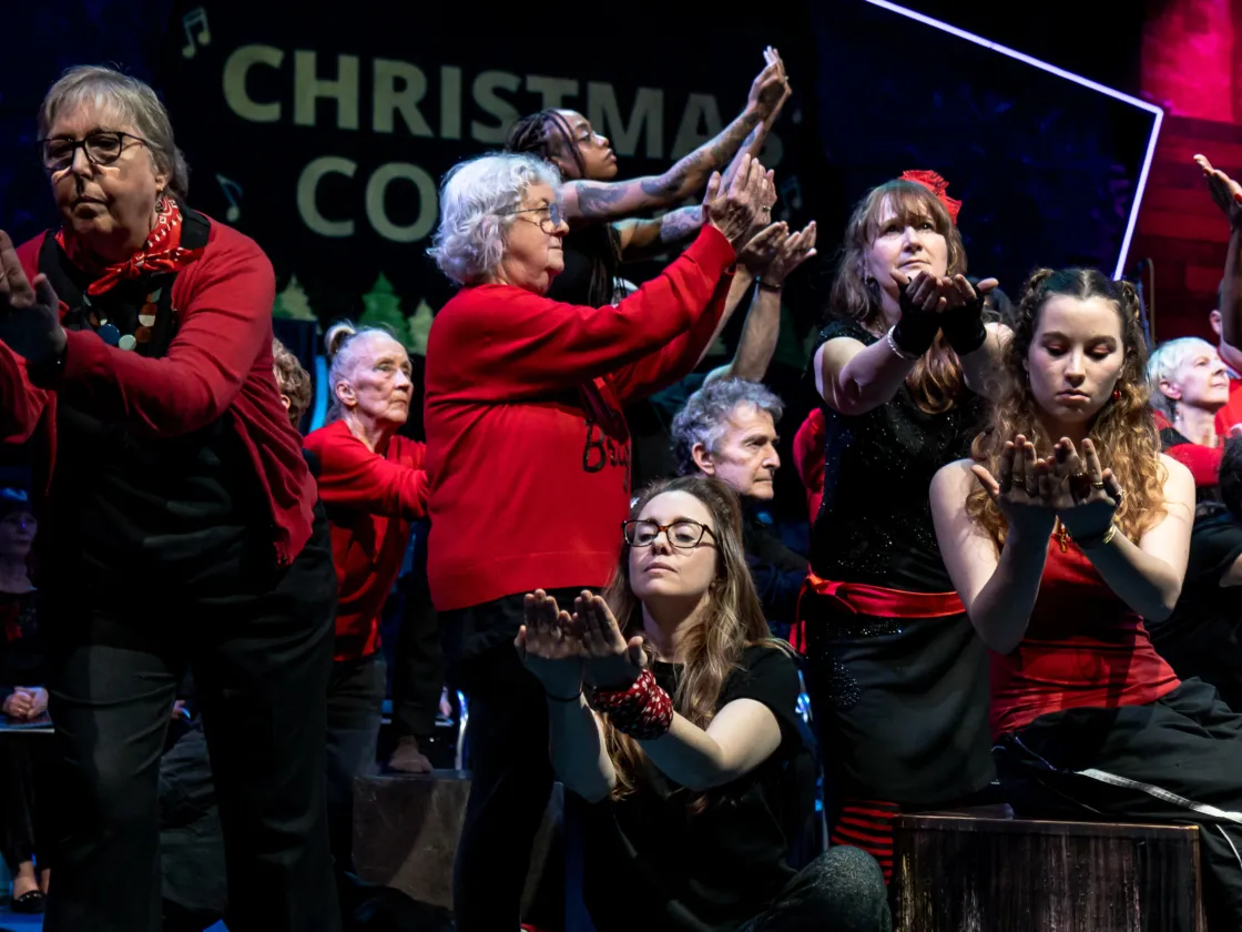 People in red and black with hands out in various poses on a stage