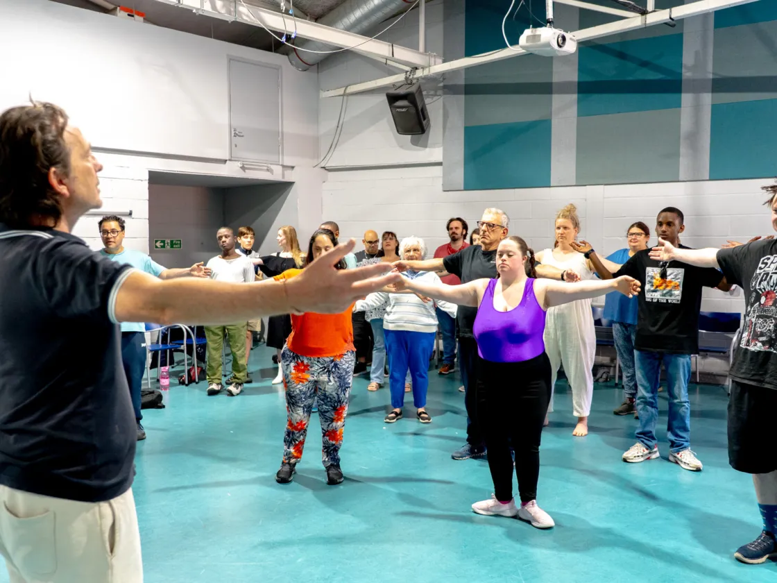 Teacher at the front of the room leading a arms out stretch to about 30 people
