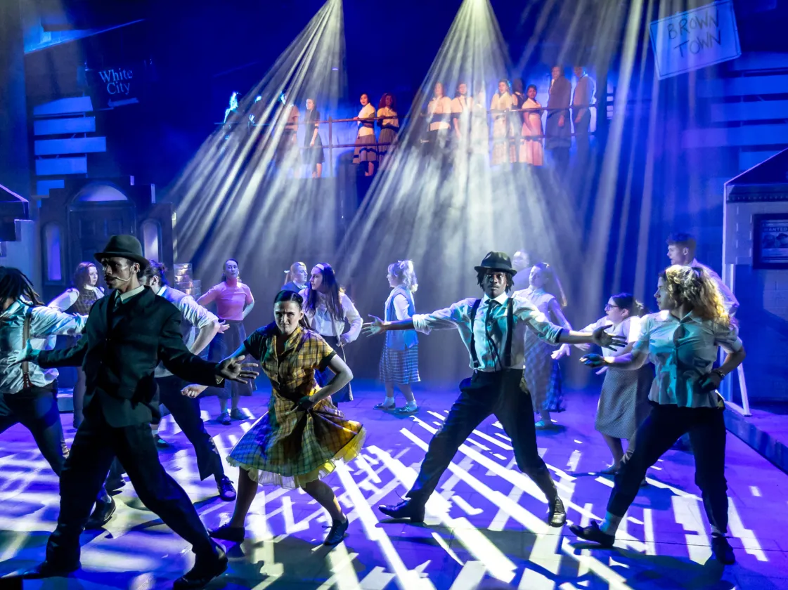 A wide-angle, full-stage photograph capturing a large cast of performers during a dynamic musical theater number.