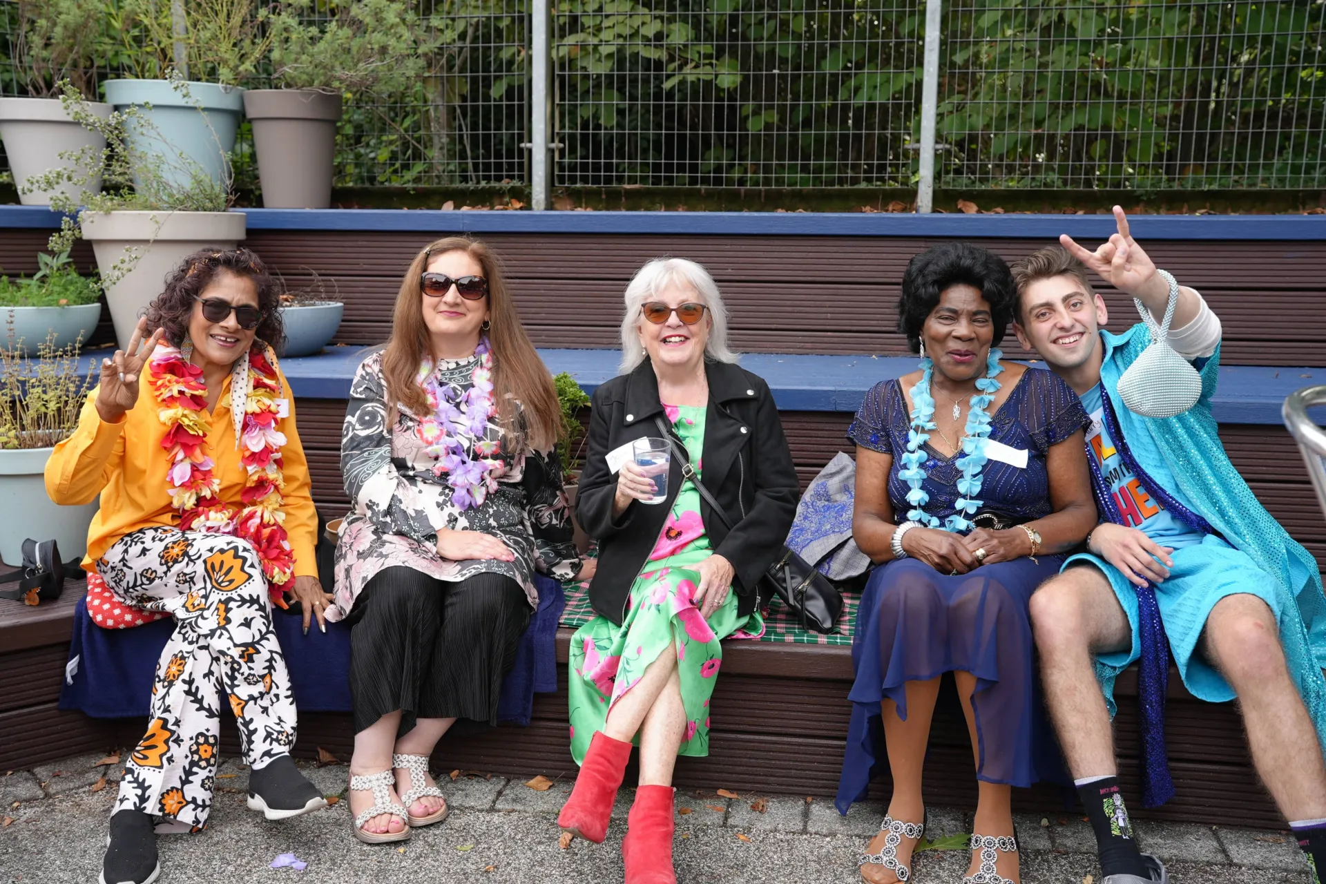 A group of Gladrags members sat outside with a younger Chickenshed member, all dressed in bright, floral festival gear.