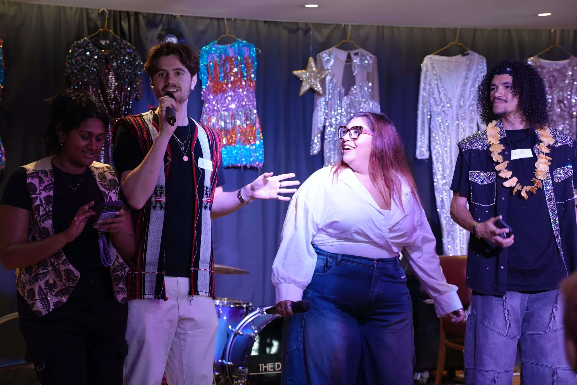 A group of Chickenshed members and staff performing inside the cafe with sparkly outfits hung behind them as decorations