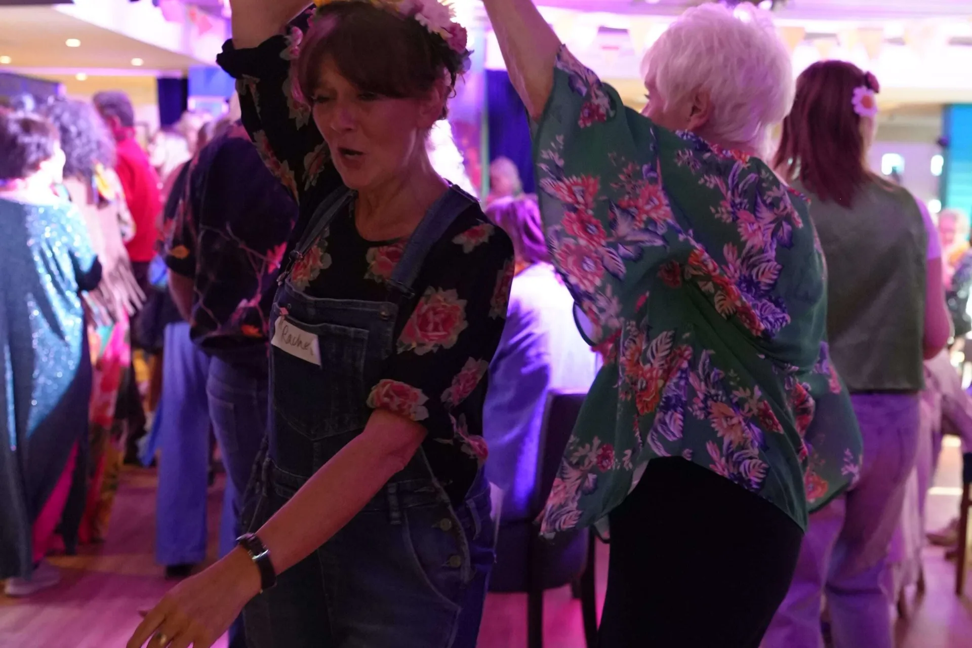 Two women wearing floral tops, one spinning the other under her arm, as they dance together on the dance floor