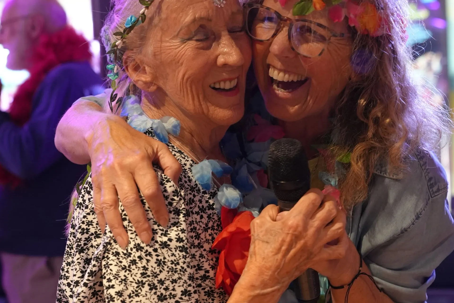 Two women wearing flower crowns and flower necklaces, hugging as they dance together on the dancefloor