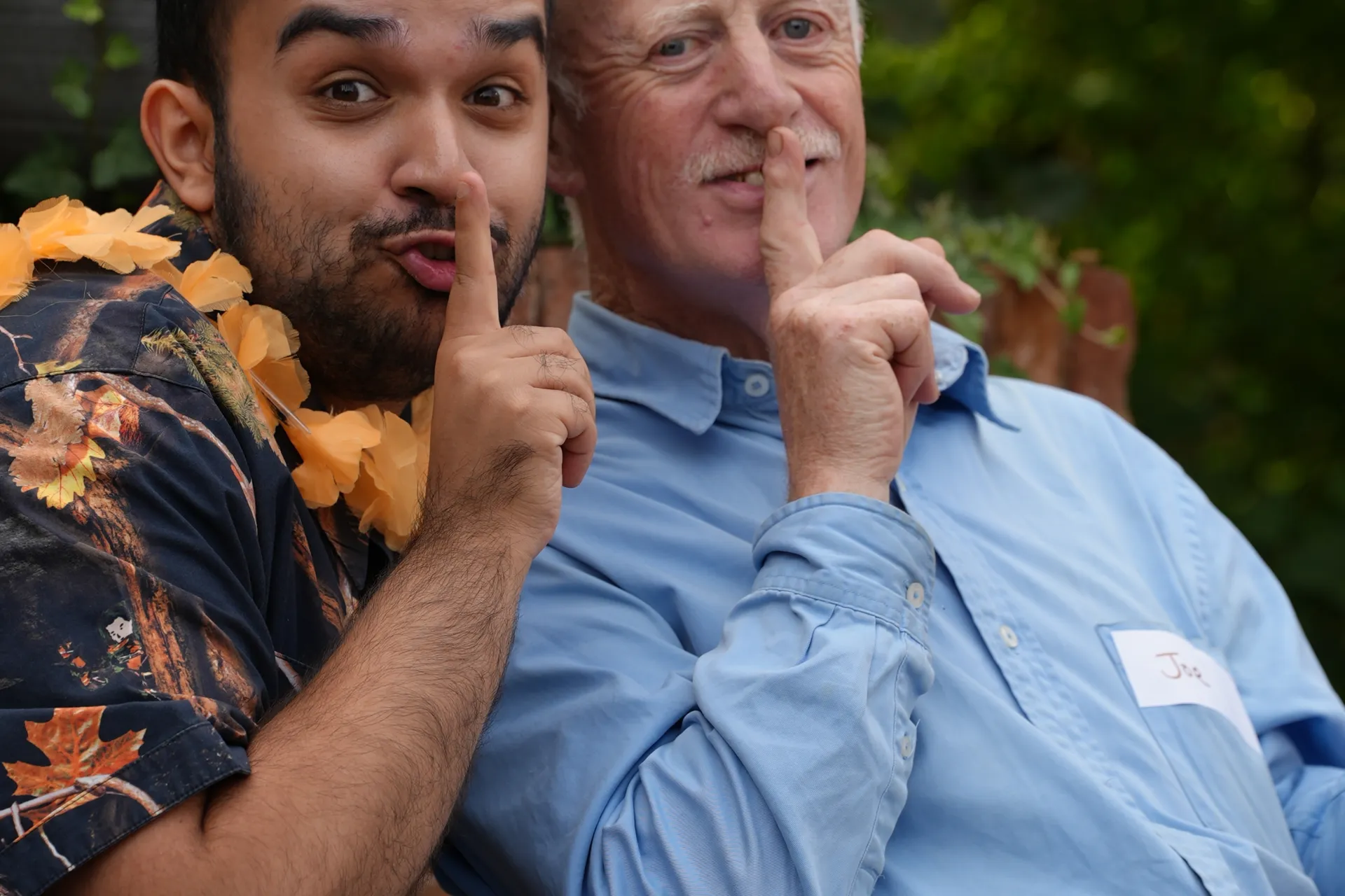 A younger Chickenshed member and a Gladrags member, holding a finger up to their lips to look like they are shushing the camera.