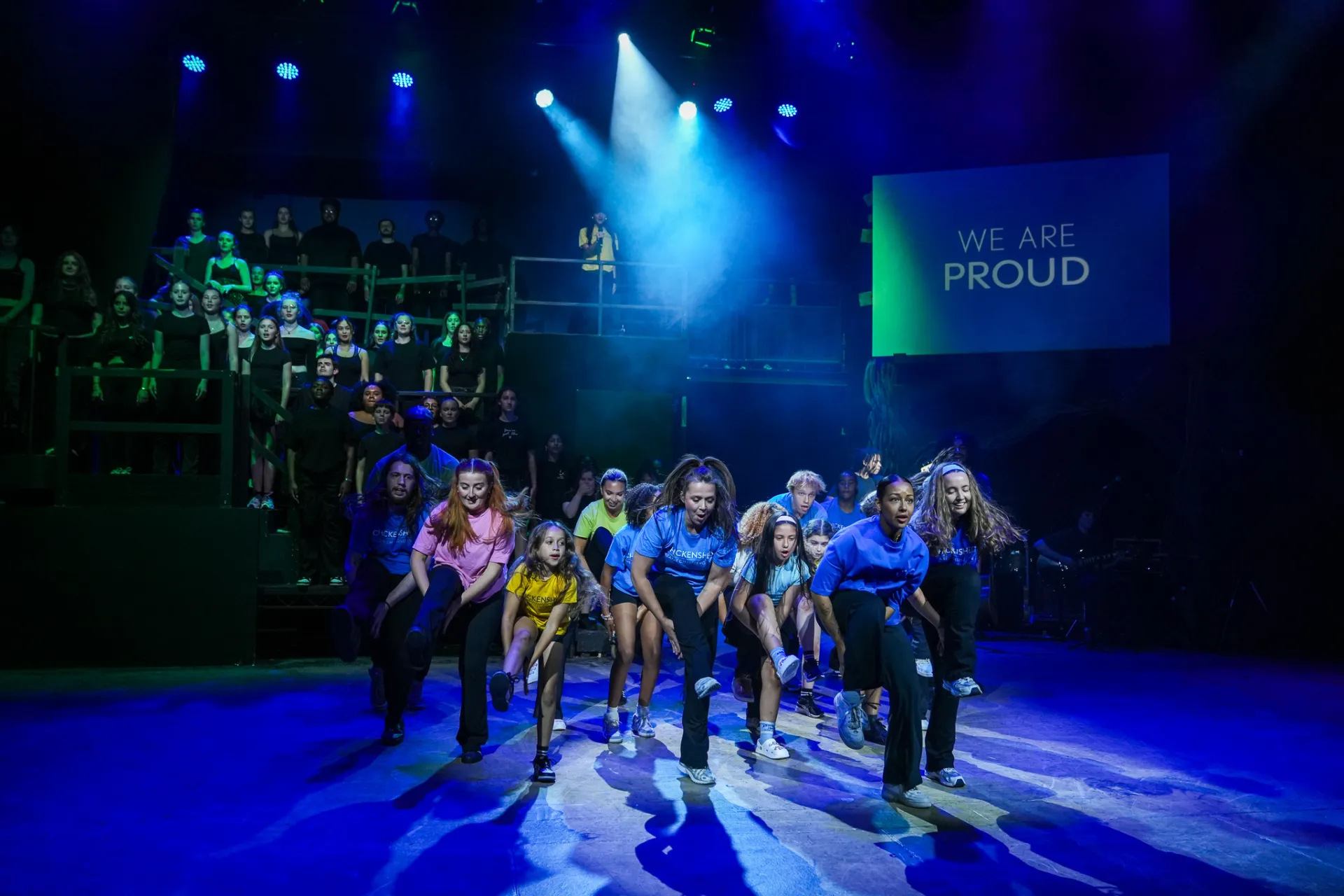 group of performers mid dance on stage with chorus of singers lifted onto back of stage
