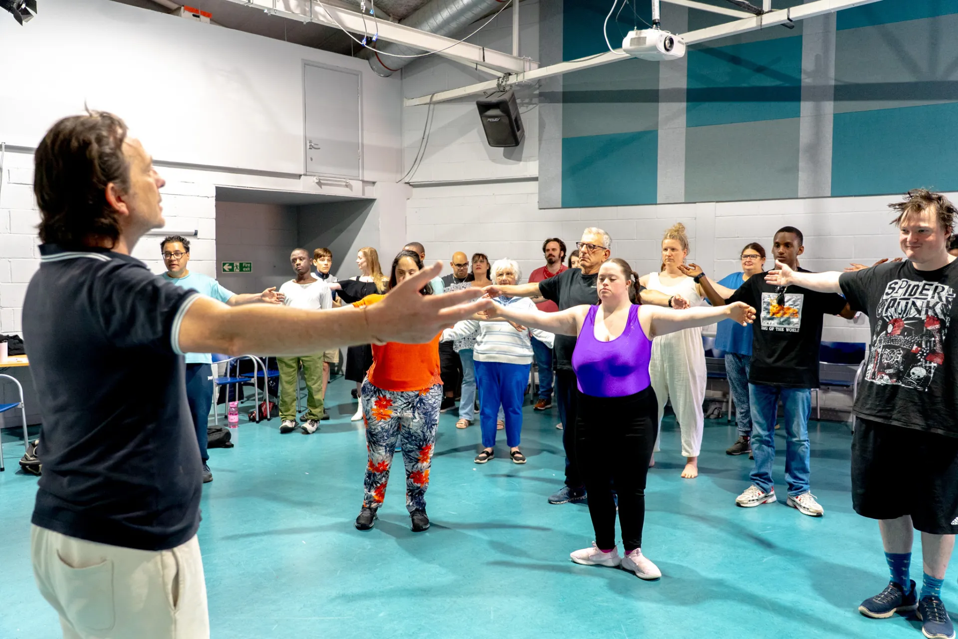 Teacher at the front of the room leading a arms out stretch to about 30 people