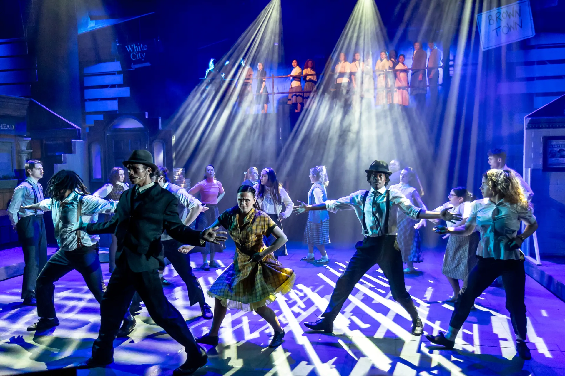 A wide-angle, full-stage photograph capturing a large cast of performers during a dynamic musical theater number.