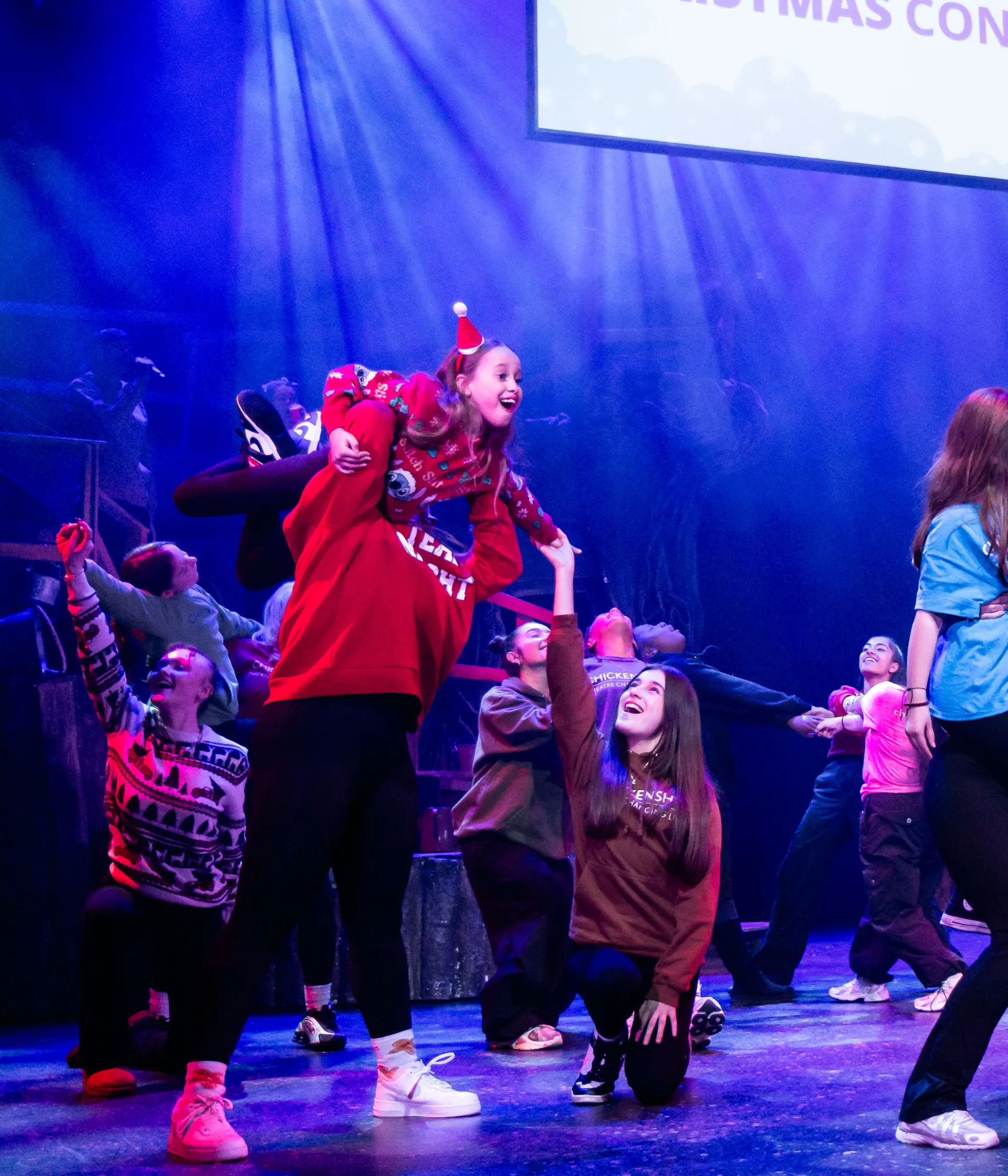 Young people on stage in colourful Christmas outfits performing Christmas songs